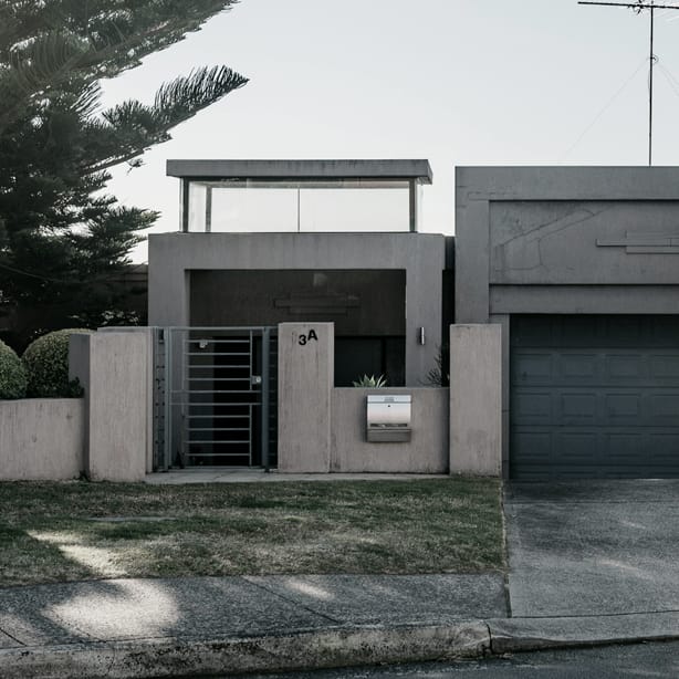 The original home before its duplex conversion: a grey rendered front wall with a steel gate, letterbox and double garage facing the street