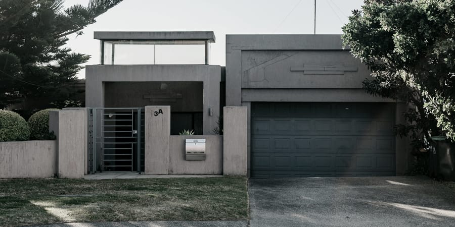 The original home before its duplex conversion: a grey rendered front wall with a steel gate, letterbox and double garage facing the street