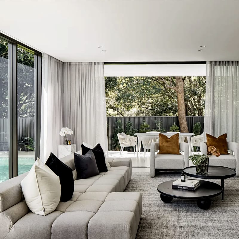Living room with a modular sofa and round coffee tables, opening through glass to a garden and pool