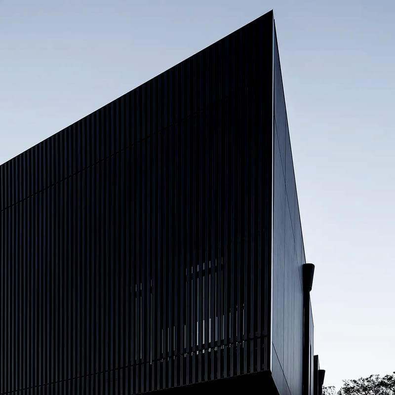 Upward view of the sharp-edged dark battened facade against a clear sky