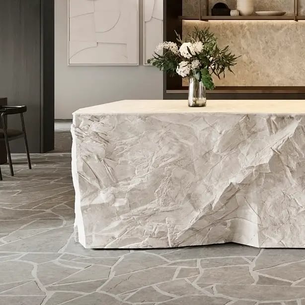 Kitchen with a rough-hewn stone island bench, crazy-paved stone floor, dark timber joinery and a dining table beyond