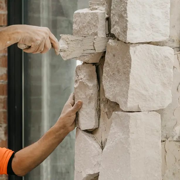 A stonemason setting rough-cut sandstone blocks into a feature wall on a residential building site