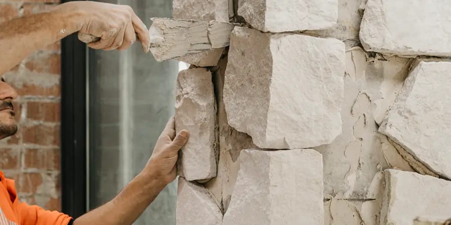 A stonemason setting rough-cut sandstone blocks into a feature wall on a residential building site